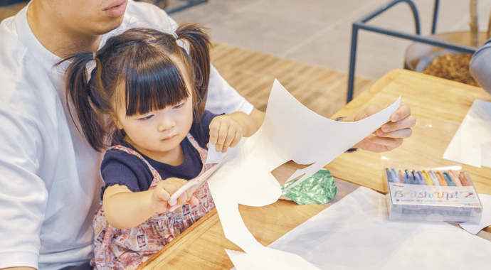 お父さんの膝の上で紙を切る女の子の写真